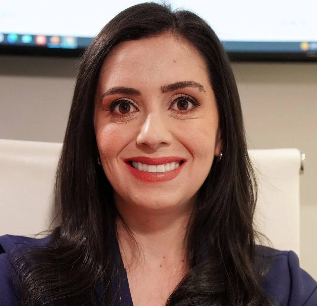 Laila Bomtempo sorrindo, de blazer azul-marinho, no consultório